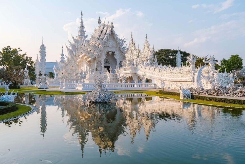 Wat Rong Khun White Temple in Chiang Rai with ornate carvings, mirrored details, and reflection in the surrounding pond.
