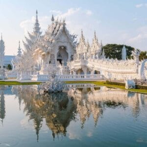 Wat Rong Khun White Temple in Chiang Rai with ornate carvings, mirrored details, and reflection in the surrounding pond.