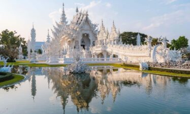 Wat Rong Khun White Temple in Chiang Rai with ornate carvings, mirrored details, and reflection in the surrounding pond.