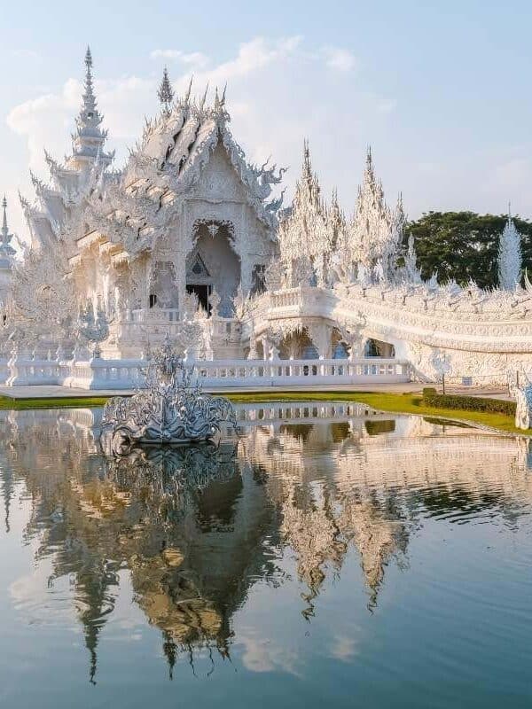 Wat Rong Khun White Temple in Chiang Rai with ornate carvings, mirrored details, and reflection in the surrounding pond.