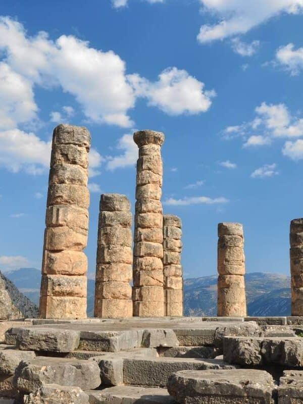 Columnas de piedra del Templo de Apolo en Delfos, Grecia, con las montañas y un cielo azul brillante de fondo.