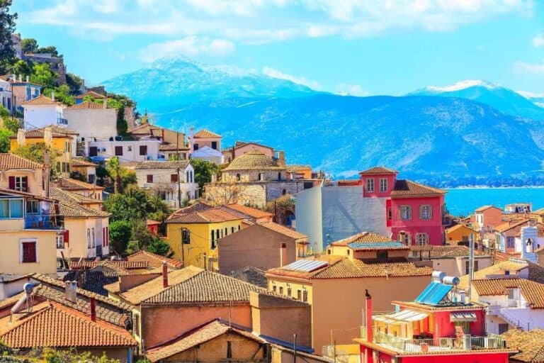 Colorful houses of Nafplio, Greece with terracotta roofs overlooking the sea and mountains under a bright blue sky.