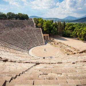 Panoramic view of the Ancient Theatre of Epidaurus with stone seating and scenic mountain backdrop in Greece.