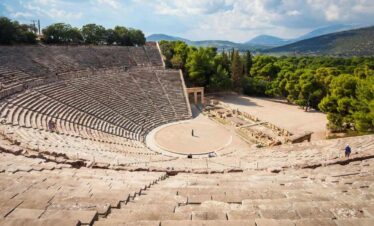 Panoramic view of the Ancient Theatre of Epidaurus with stone seating and scenic mountain backdrop in Greece.