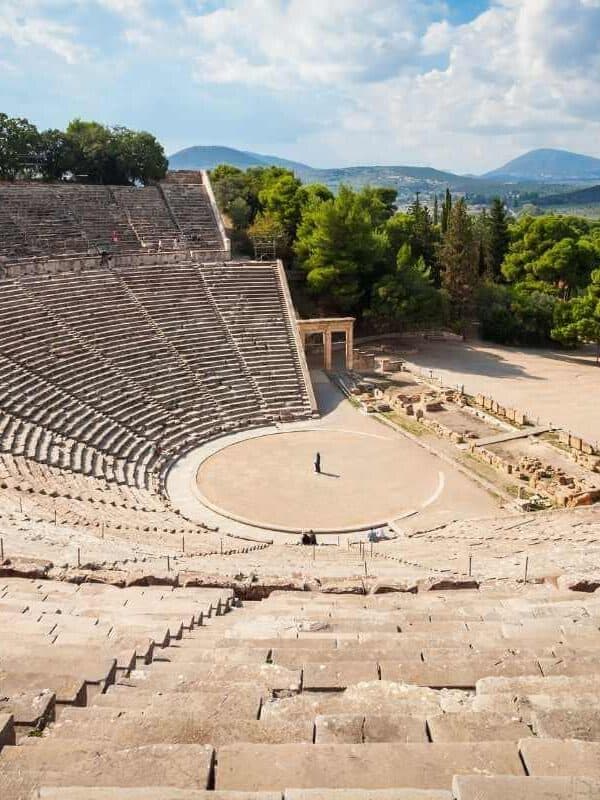 Panoramic view of the Ancient Theatre of Epidaurus with stone seating and scenic mountain backdrop in Greece.