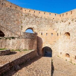 Ancient stone walls and arched gateways of Palamidi Fortress in Nafplio, Greece, under a bright blue sky.
