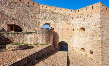 Ancient stone walls and arched gateways of Palamidi Fortress in Nafplio, Greece, under a bright blue sky.