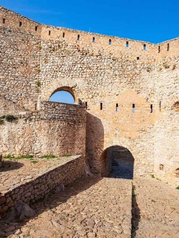 Ancient stone walls and arched gateways of Palamidi Fortress in Nafplio, Greece, under a bright blue sky.