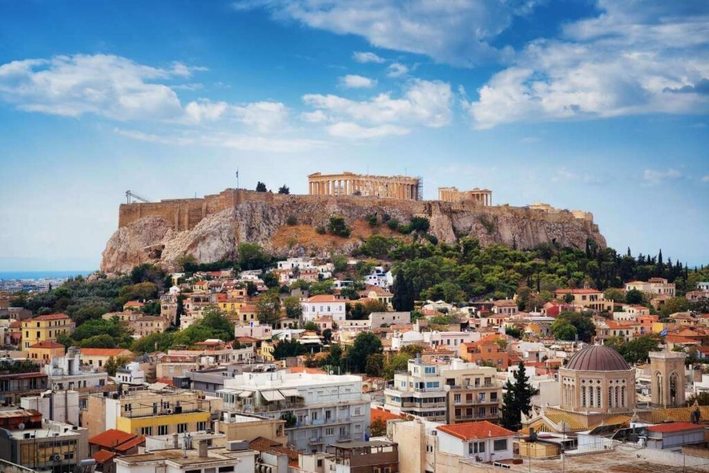 Scenic view of the Acropolis of Athens, Greece, with the Parthenon overlooking colorful city buildings and greenery.