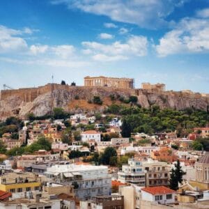 Scenic view of the Acropolis of Athens, Greece, with the Parthenon overlooking colorful city buildings and greenery.