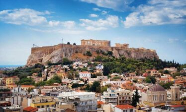 Scenic view of the Acropolis of Athens, Greece, with the Parthenon overlooking colorful city buildings and greenery.
