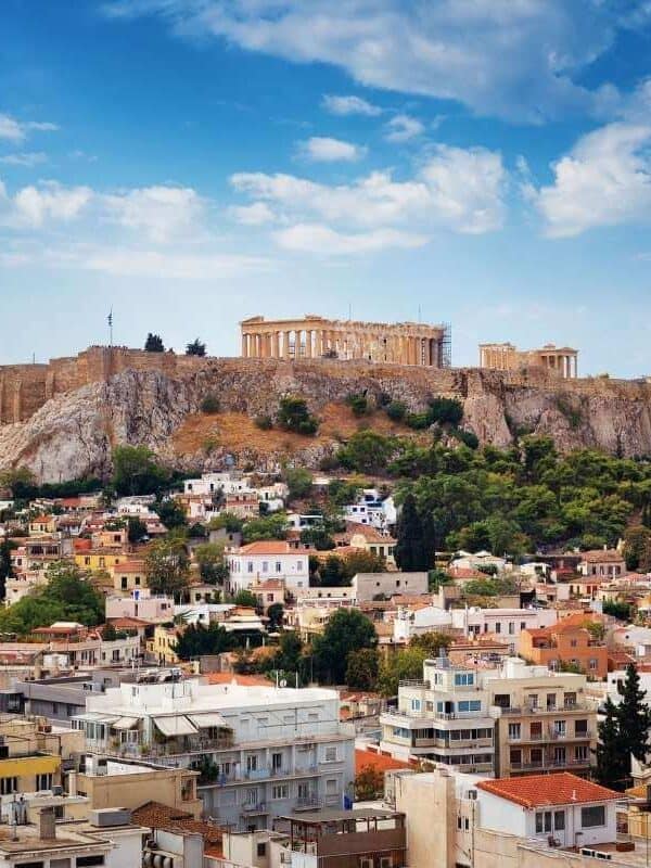 Scenic view of the Acropolis of Athens, Greece, with the Parthenon overlooking colorful city buildings and greenery.
