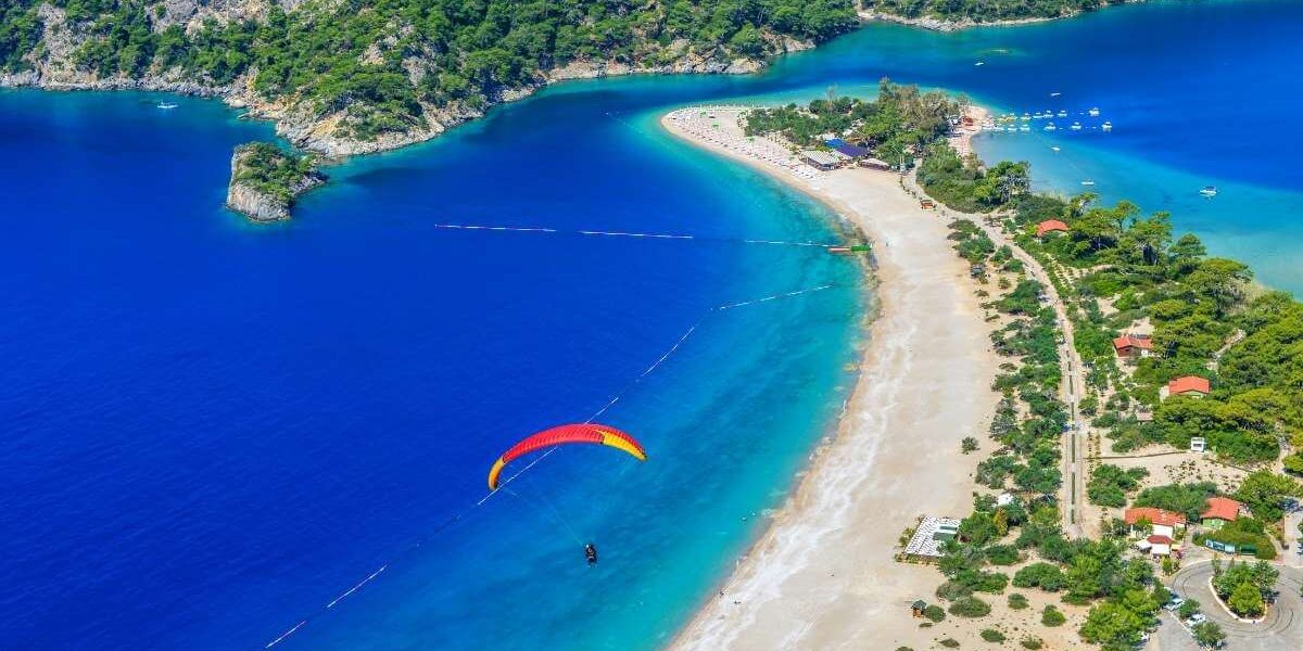 Aerial view of Ölüdeniz Beach in Turkey with turquoise water, lush green hills, and a paraglider soaring above the blue lagoon.