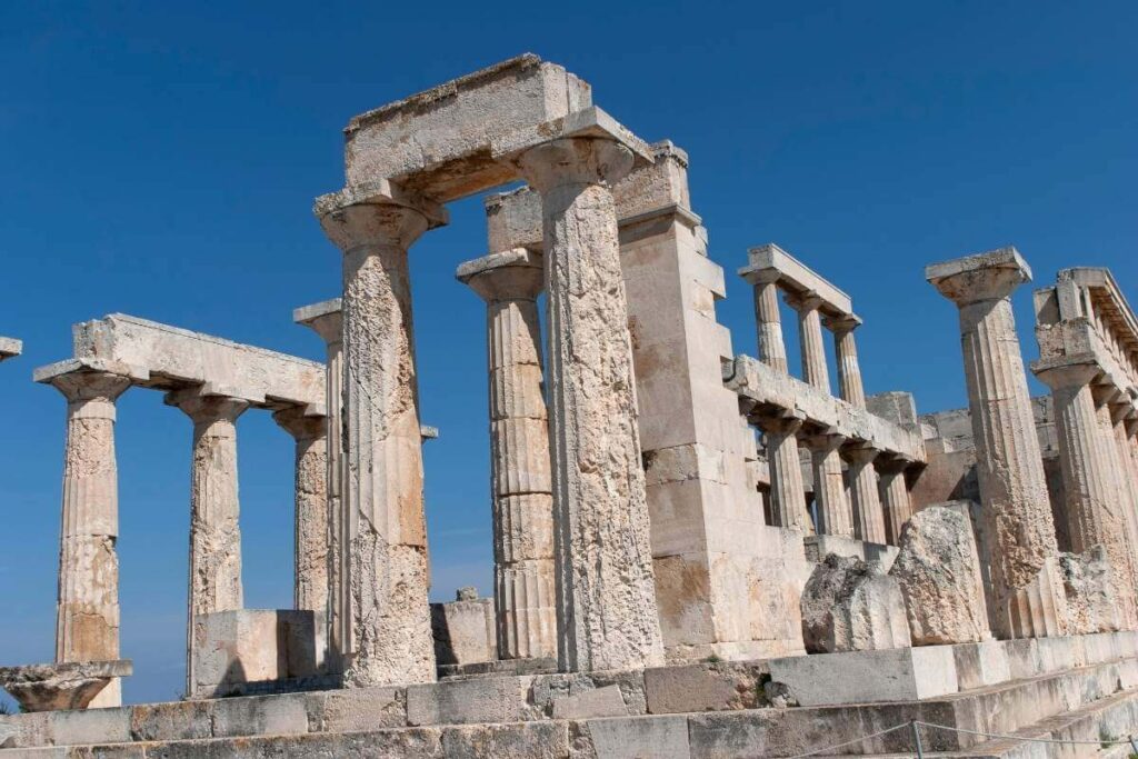 Ancient stone columns and ruins of the Temple of Aphaia on Aegina Island under a clear blue sky.