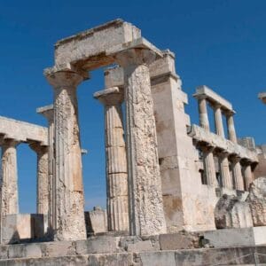Ancient stone columns and ruins of the Temple of Aphaia on Aegina Island under a clear blue sky.