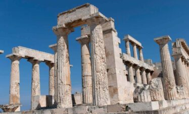Ancient stone columns and ruins of the Temple of Aphaia on Aegina Island under a clear blue sky.