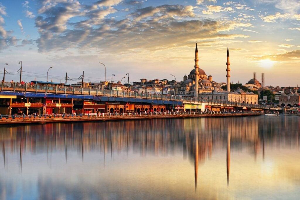 Golden sunset over Istanbul’s Galata Bridge with the New Mosque reflecting on calm waters, showcasing a vibrant cityscape.