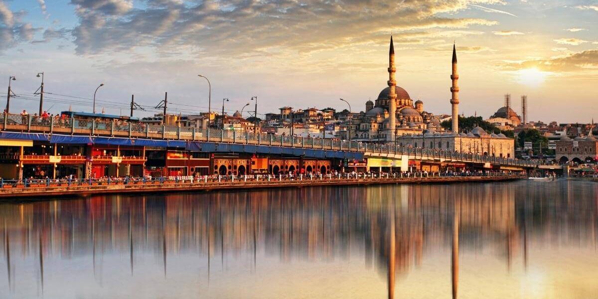 Golden sunset over Istanbul’s Galata Bridge with the New Mosque reflecting on calm waters, showcasing a vibrant cityscape.