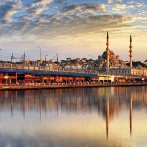 Golden sunset over Istanbul’s Galata Bridge with the New Mosque reflecting on calm waters, showcasing a vibrant cityscape.