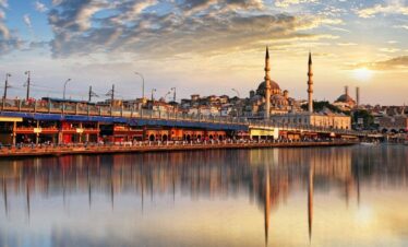 Golden sunset over Istanbul’s Galata Bridge with the New Mosque reflecting on calm waters, showcasing a vibrant cityscape.