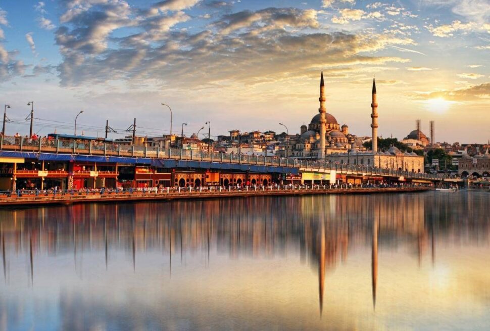 Golden sunset over Istanbul’s Galata Bridge with the New Mosque reflecting on calm waters, showcasing a vibrant cityscape.