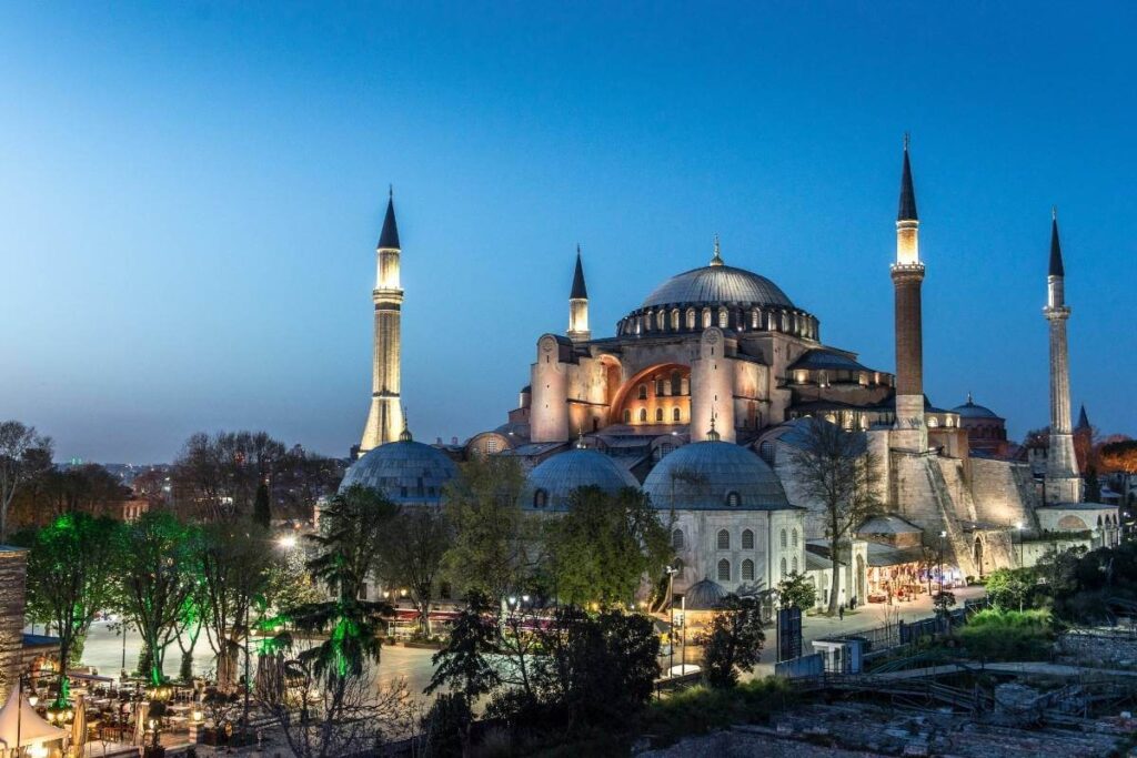 Hagia Sophia illuminated at dusk with glowing minarets and surrounding greenery, highlighting this iconic Istanbul landmark.