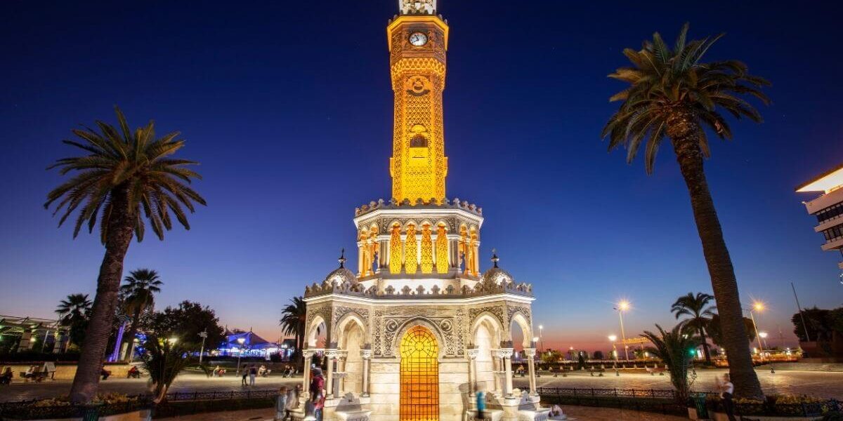 Illuminated Izmir Clock Tower at dusk with palm trees and deep blue sky in Konak Square, Turkey.