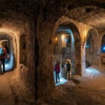 Tourists with flashlights exploring the deep stone tunnels of Derinkuyu Underground City in Cappadocia.