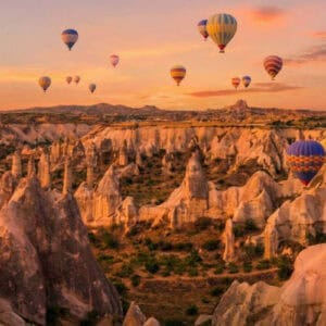 Colorful hot air balloons over Cappadocia fairy chimneys at sunrise, a highlight of scenic Turkey tours.