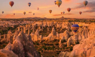 Colorful hot air balloons over Cappadocia fairy chimneys at sunrise, a highlight of scenic Turkey tours.