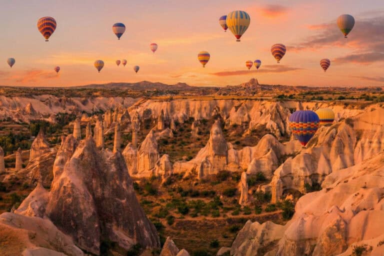 Colorful hot air balloons over Cappadocia fairy chimneys at sunrise, a highlight of scenic Turkey tours.