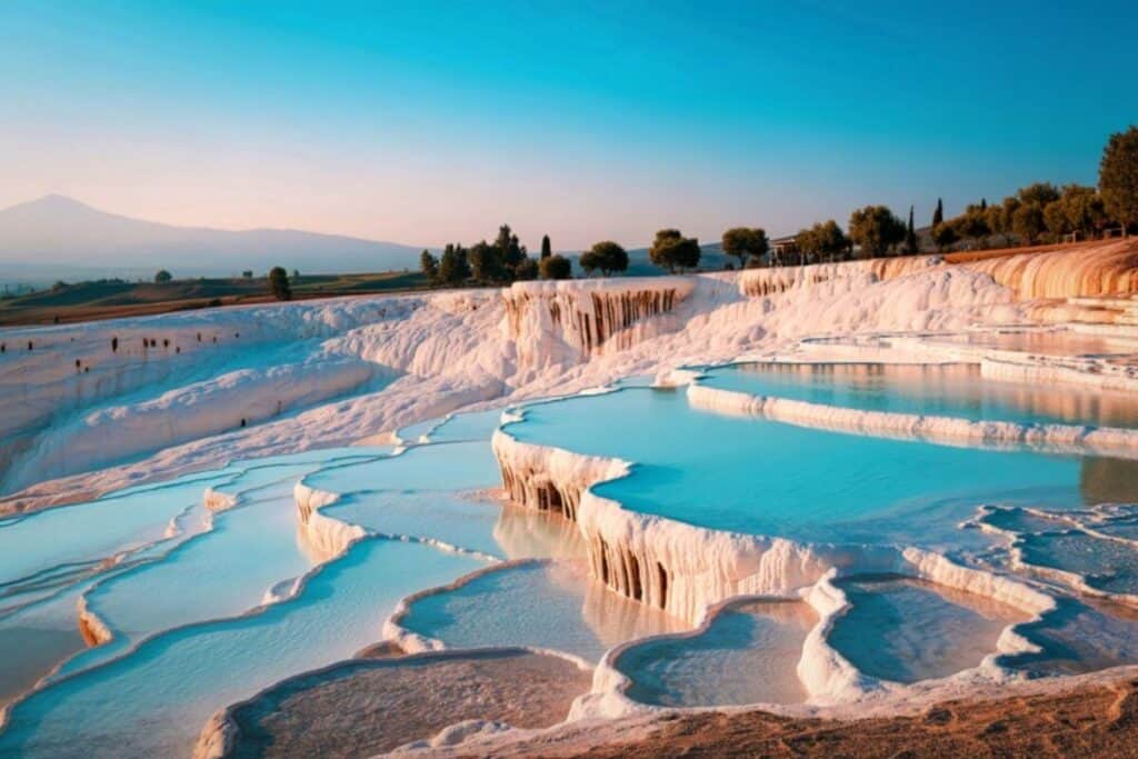 Scenic Pamukkale thermal pools featuring white travertine terraces filled with turquoise water under a clear blue sky.