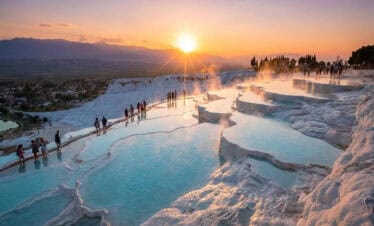Pamukkale travertines at sunset with turquoise thermal pools and visitors walking along white terraces in Denizli, Turkey