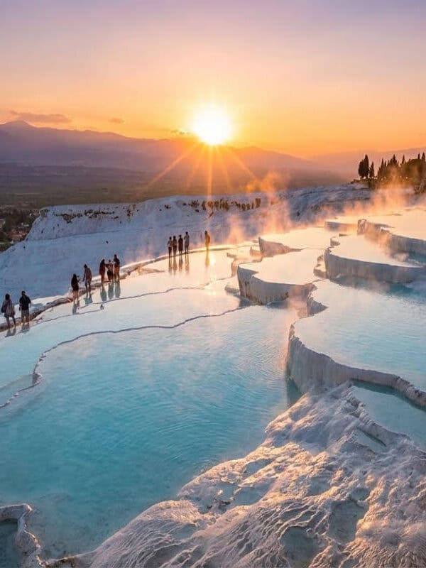 Pamukkale travertines at sunset with turquoise thermal pools and visitors walking along white terraces in Denizli, Turkey