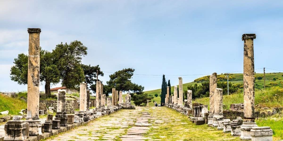 Ancient colonnaded Sacred Way street at the Asklepieion of Pergamon ruins in Bergama, Turkey, under a blue sky.