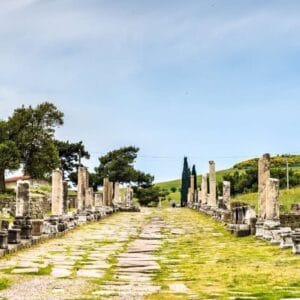 Ancient colonnaded Sacred Way street at the Asklepieion of Pergamon ruins in Bergama, Turkey, under a blue sky.