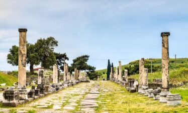 Ancient colonnaded Sacred Way street at the Asklepieion of Pergamon ruins in Bergama, Turkey, under a blue sky.