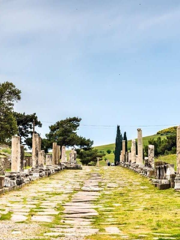 Ancient colonnaded Sacred Way street at the Asklepieion of Pergamon ruins in Bergama, Turkey, under a blue sky.