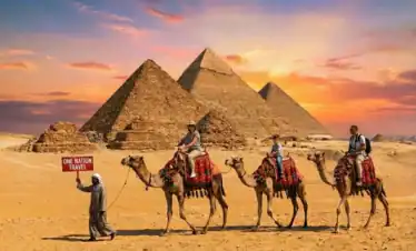 One Nation Travel guide holding a red sign leading an Egypt tour with tourists riding camels in front of the Giza Pyramids at sunset