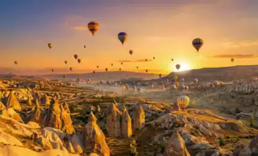 Hot air balloons flying at golden sunrise over the unique rock formations and fairy chimneys of Cappadocia, Turkey. A highlight of the Best of Turkey tour.