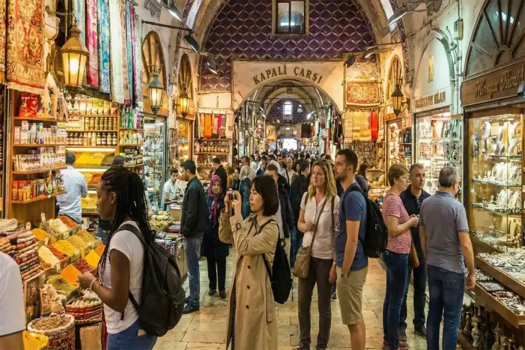 Diverse group of international tourists, including Black, Asian, and European women, exploring the historic streets and shopping for colorful lanterns at the Grand Bazaar in Istanbul.