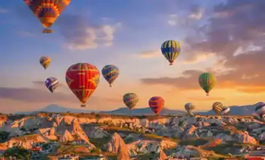 Colorful hot air balloons floating over the rocky fairy chimneys of Cappadocia, Turkey during a stunning sunrise.