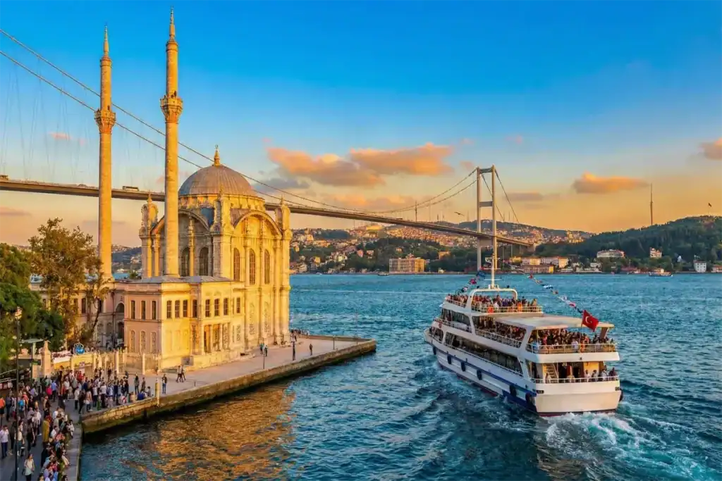 A scenic Bosphorus cruise boat sailing past the historic Ortaköy Mosque and the Bosphorus Bridge at sunset, offering the best views of Istanbul between Europe and Asia.