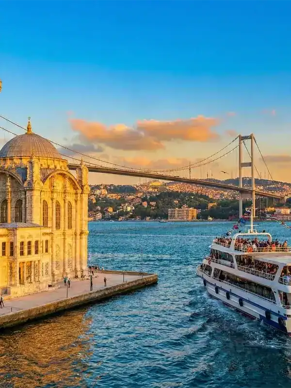 A scenic Bosphorus cruise boat sailing past the historic Ortaköy Mosque and the Bosphorus Bridge at sunset, offering the best views of Istanbul between Europe and Asia.