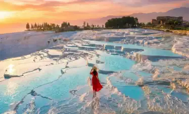 A traveler in a red dress admiring the sunset view over the turquoise thermal pools and white travertine terraces of Pamukkale, a highlight included in the 4 Days Cappadocia and Pamukkale Tour from Istanbul.