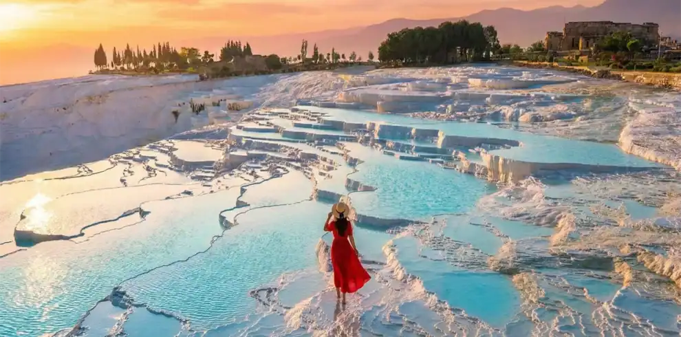 A traveler in a red dress admiring the sunset view over the turquoise thermal pools and white travertine terraces of Pamukkale, a highlight included in the 4 Days Cappadocia and Pamukkale Tour from Istanbul.