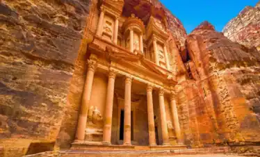 The iconic Treasury (Al-Khazneh) facade intricately carved into red sandstone cliffs under a clear blue sky in the ancient city of Petra, Jordan.