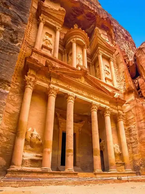 The iconic Treasury (Al-Khazneh) facade intricately carved into red sandstone cliffs under a clear blue sky in the ancient city of Petra, Jordan.
