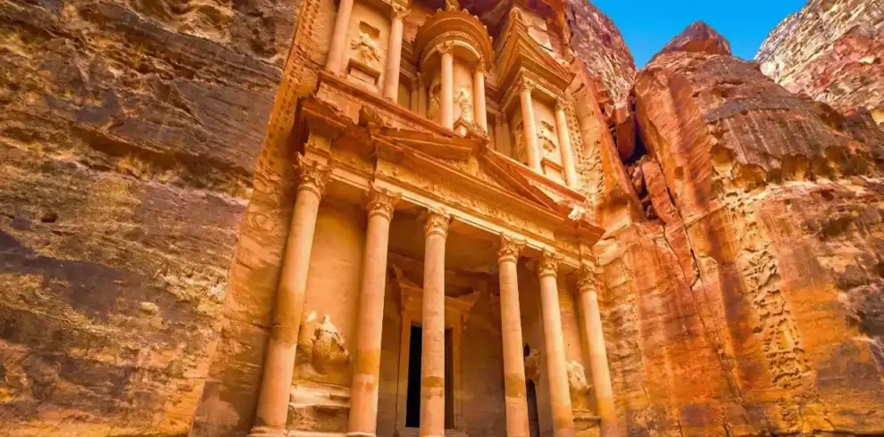 The iconic Treasury (Al-Khazneh) facade intricately carved into red sandstone cliffs under a clear blue sky in the ancient city of Petra, Jordan.