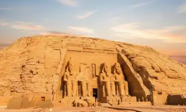 A panoramic sunset view over the Nile River featuring the Great Pyramids of Giza, the Sphinx, a luxury river cruise ship, felucca sailboats, and an ancient temple on the bank. This scene highlights major destinations included in the "10 Days Wonders of Egypt Tour from New York" itinerary.